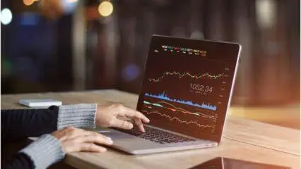 Persona analizando datos del mercado de valores en una computadora portátil. Se muestra 1052.34.