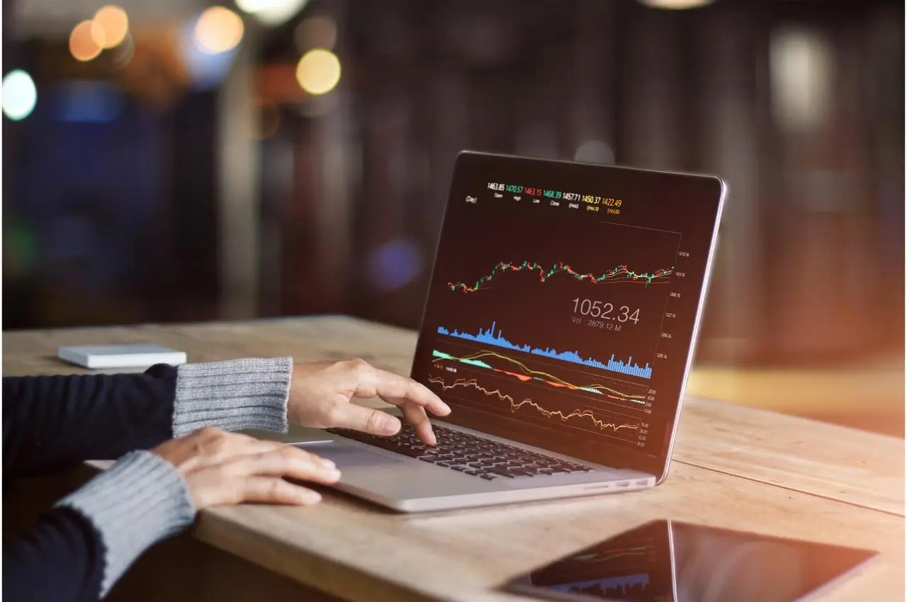 Persona analizando datos del mercado de valores en una computadora portátil. Se muestra 1052.34.