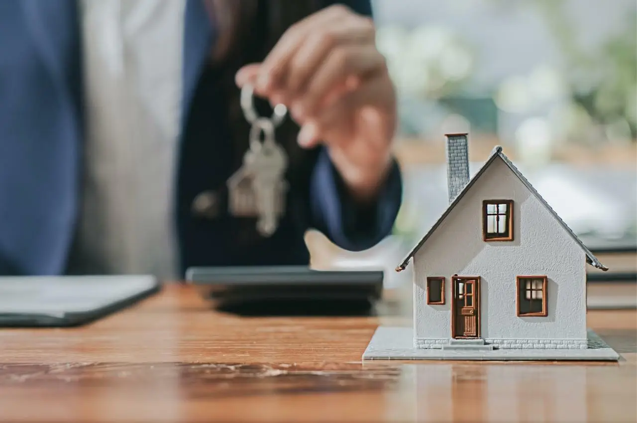 Agente inmobiliario entregando llaves de casa y casa modelo