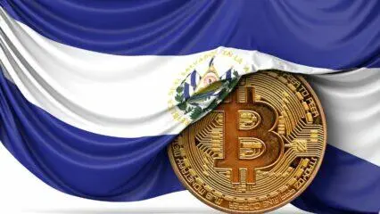 Moneda Bitcoin bajo la bandera de El Salvador; aventura en El Salvador con Bitcoin.
