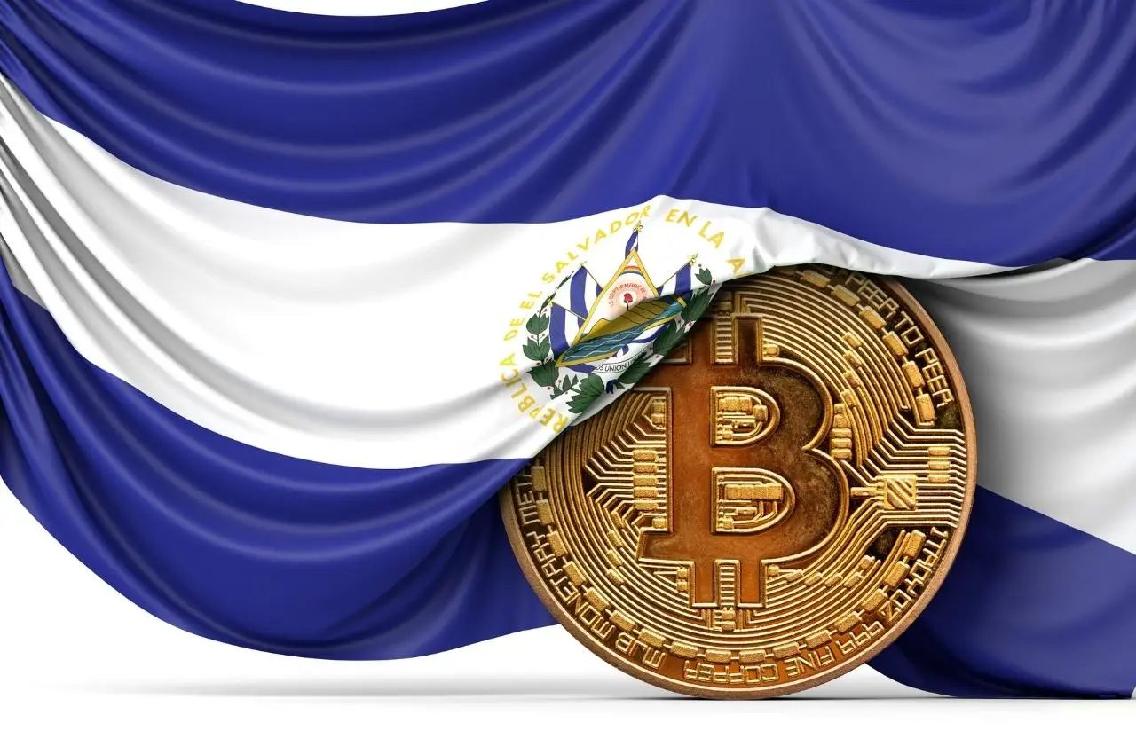 Moneda Bitcoin bajo la bandera de El Salvador; aventura en El Salvador con Bitcoin.