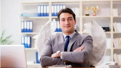 Empresario con alas de ángel sentado en un escritorio, con los brazos cruzados. Inversión en una startup peruana.