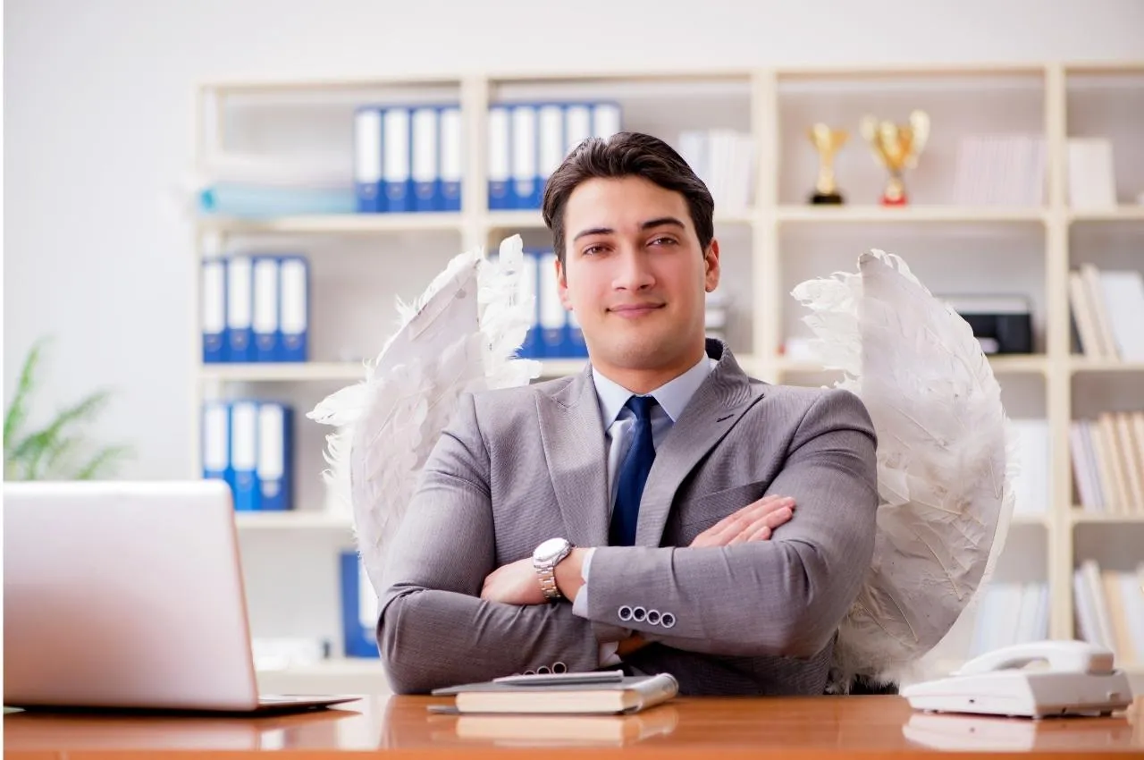 Empresario con alas de ángel sentado en un escritorio, con los brazos cruzados. Inversión en una startup peruana.