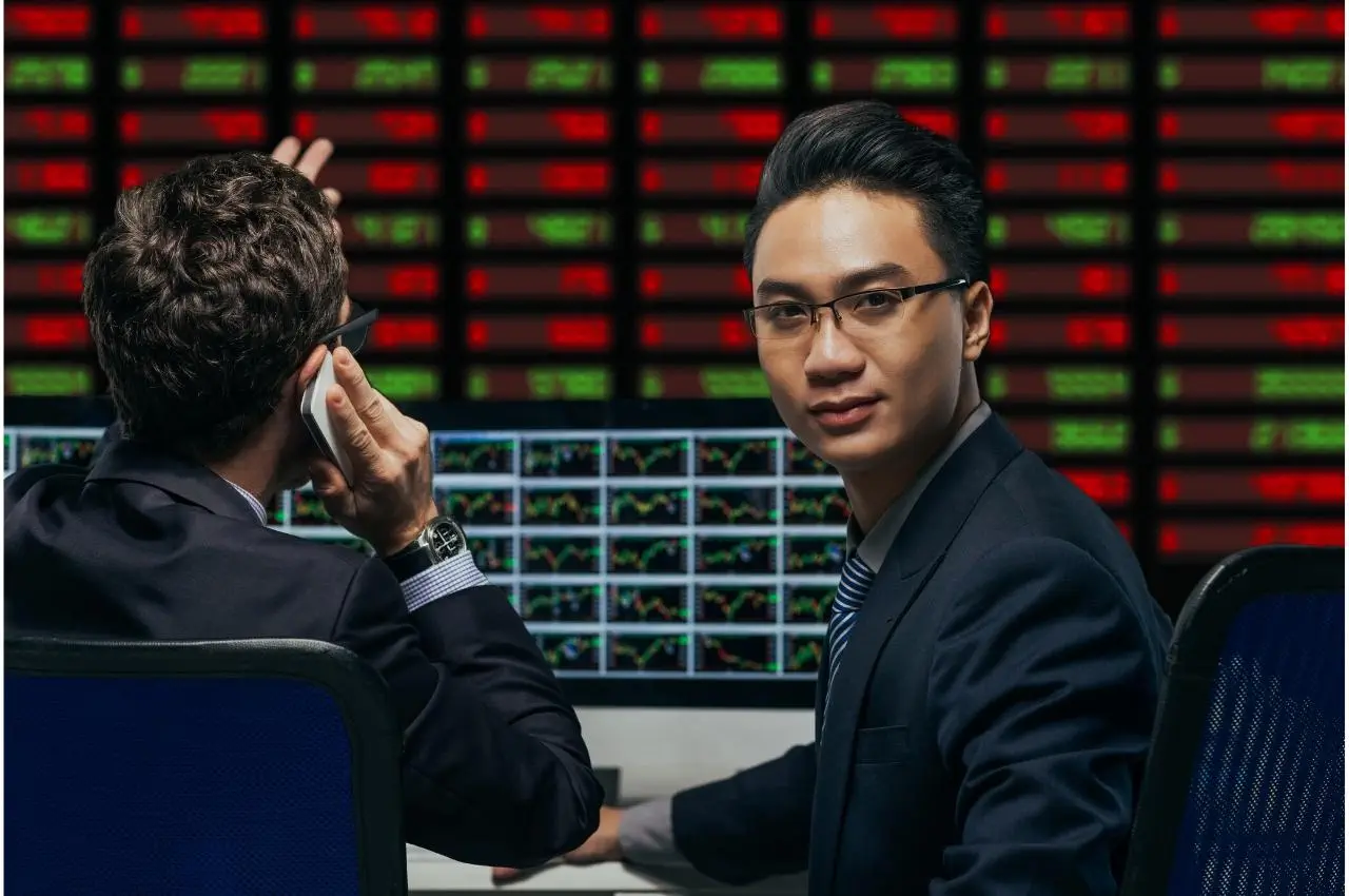 Dos corredores trabajan frente a pantallas de ordenador, analizando datos del mercado bursátil. Elegir el corredor adecuado es clave.