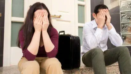 Pareja disgustada sentada en las escaleras con una maleta, enfrentándose a una ejecución hipotecaria. Evitar embargo hipotecario.