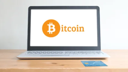 Laptop con el logo de Bitcoin y tarjeta de crédito sobre un escritorio de madera. Compra Bitcoin en Perú.