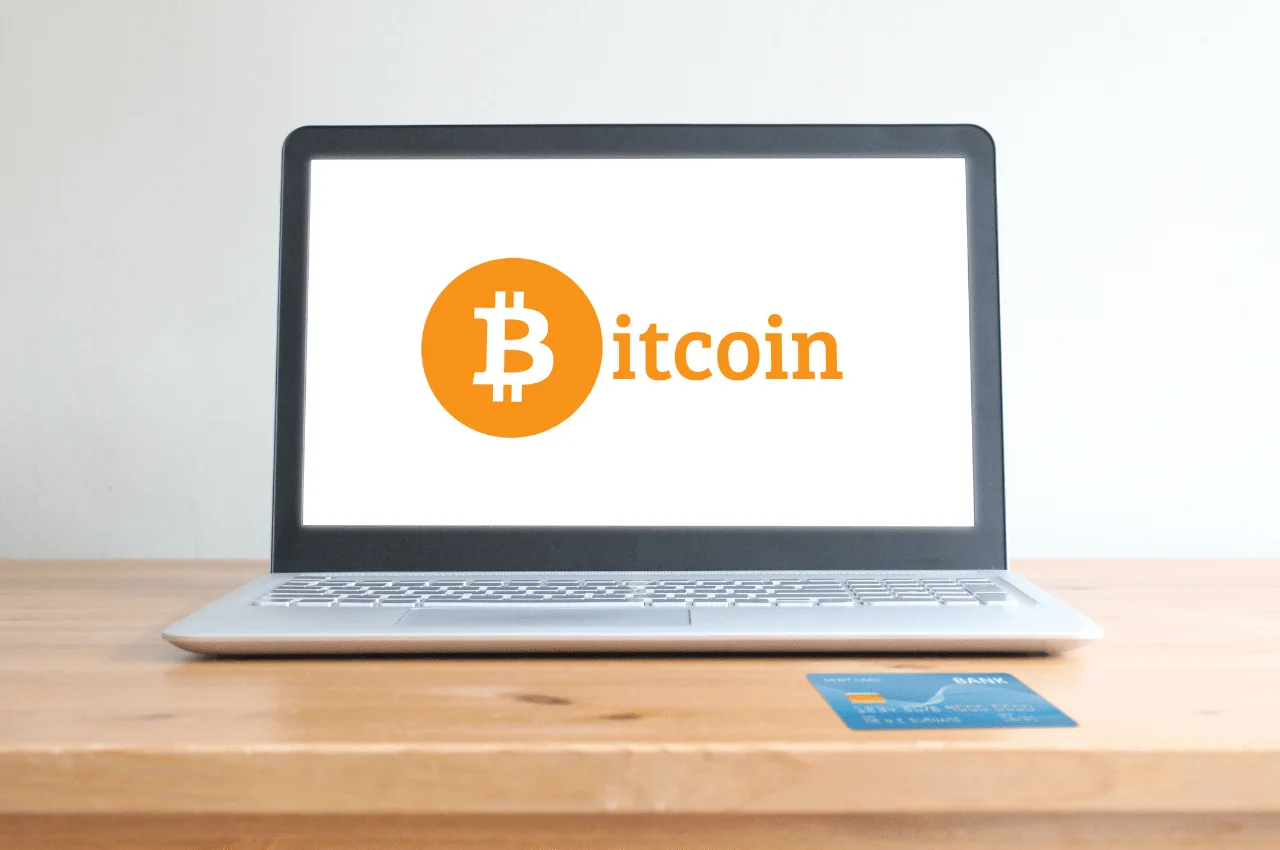 Laptop con el logo de Bitcoin y tarjeta de crédito sobre un escritorio de madera. Compra Bitcoin en Perú.