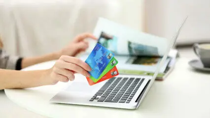 Mujer usando una laptop para comprar en línea, con tarjetas de crédito en la mano. Eligiendo la mejor pasarela de pago para comercio electrónico.