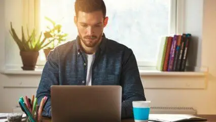 Hombre trabajando con una computadora portátil en casa, concentrado en su blog.