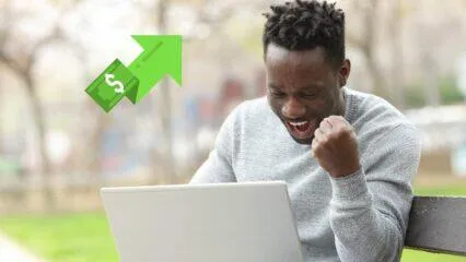 Un hombre emocionado celebra las ganancias del mercado de valores en una computadora portátil.