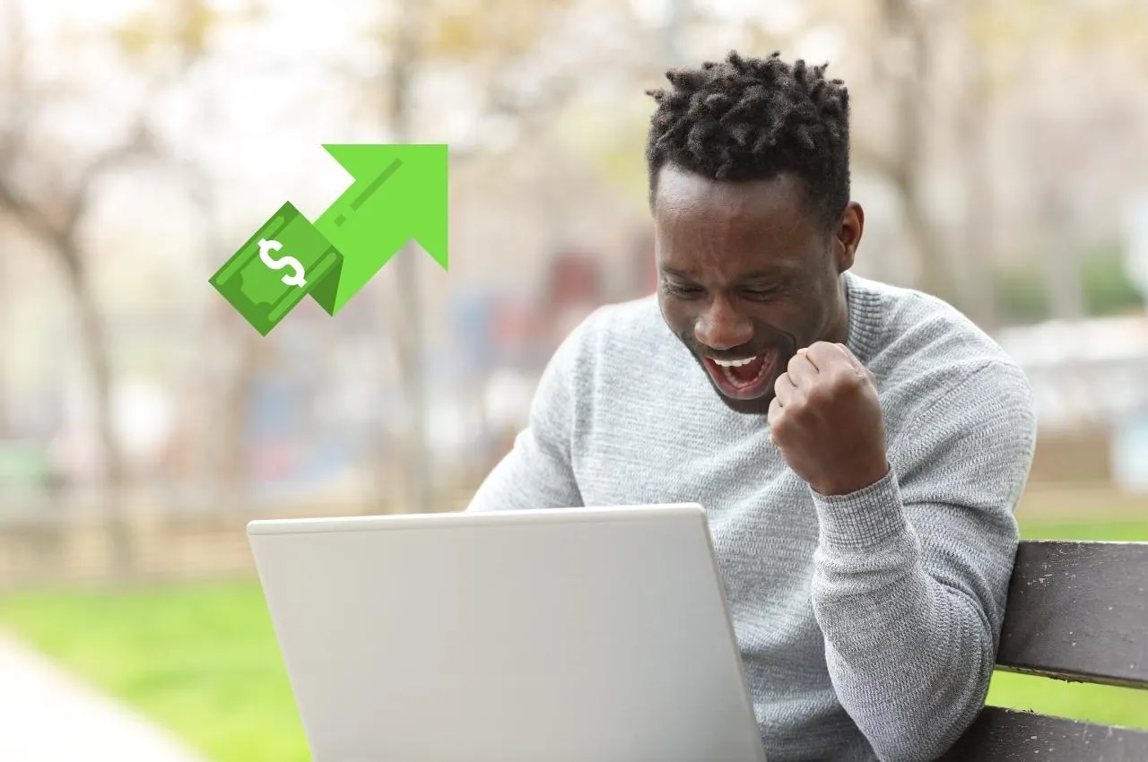 Un hombre emocionado celebra las ganancias del mercado de valores en una computadora portátil.
