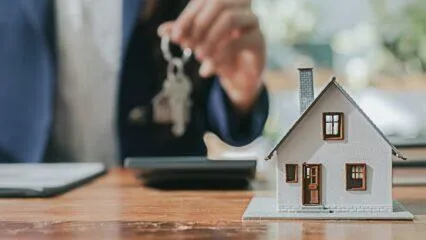 Agente inmobiliario entregando llaves de casa y casa modelo