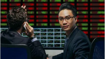 Dos corredores trabajan frente a pantallas de ordenador, analizando datos del mercado bursátil. Elegir el corredor adecuado es clave.