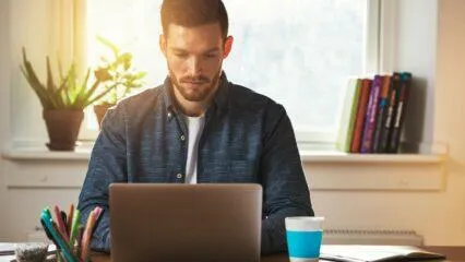 Hombre trabajando con una computadora portátil en casa, concentrado en su blog.