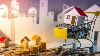 Casa en miniatura en un carrito de compras lleno de monedas, que representa oportunidades de inversión inmobiliaria.