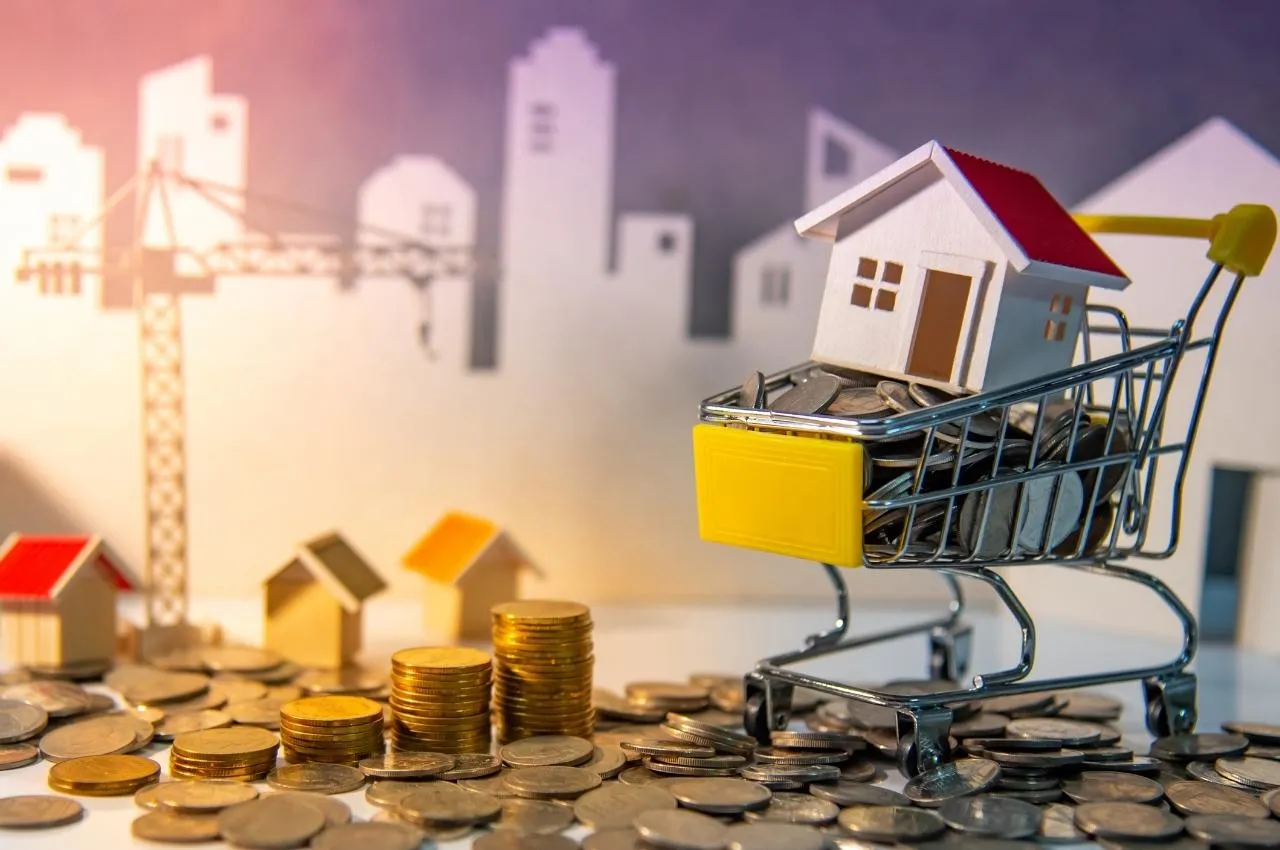 Casa en miniatura en un carrito de compras lleno de monedas, que representa oportunidades de inversión inmobiliaria.