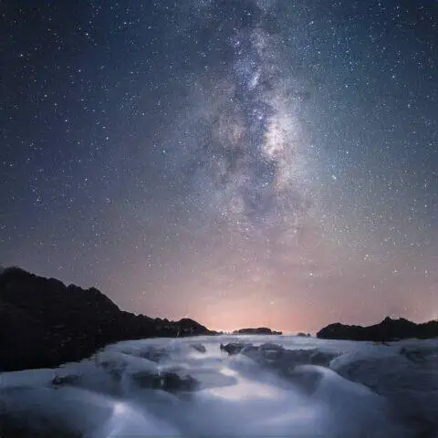 Galaxia de la Vía Láctea sobre un tranquilo río cubierto de nieve por la noche.