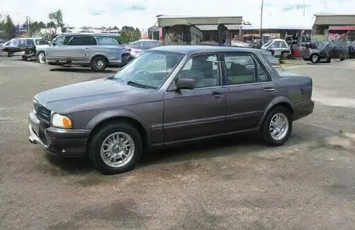 Sedán gris oscuro de los años 90 estacionado en un estacionamiento