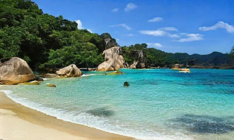 Playa tropical aislada con agua turquesa, rocas de granito y exuberante follaje verde.