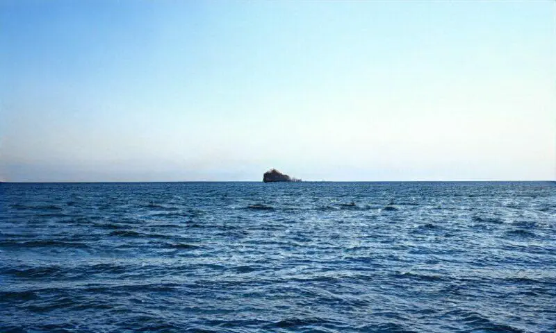 Isla solitaria en un océano en calma bajo un cielo azul claro.