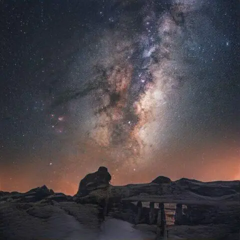 Galaxia de la Vía Láctea sobre formaciones rocosas cubiertas de nieve por la noche.