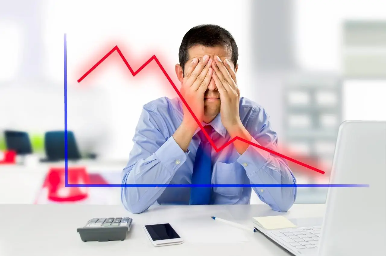 Empresario estresado cubriéndose los ojos con un gráfico de tendencia bajista superpuesto. ¡Evita estos errores comunes en el mercado de valores!