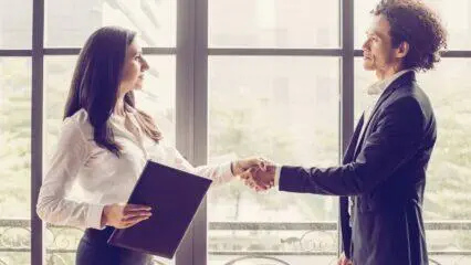 Socios comerciales se dan la mano cerca de una ventana, lo que significa una asociación exitosa.