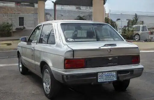 Un Ford Festiva hatchback color plata estacionado en un estacionamiento.