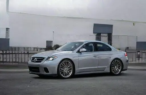 Coche deportivo plateado de la marca Acura, modelo CL, estacionado en una calle urbana. Se destacan sus llantas de aleación y diseño aerodinámico. Fondo industrial con edificios y pavimento.