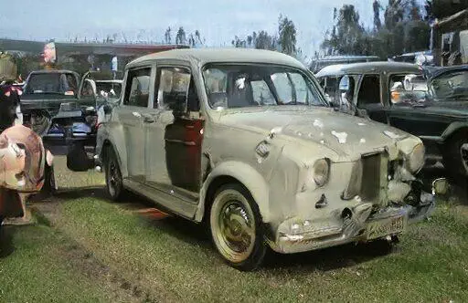 Auto clásico en un evento de exhibición de vehículos antiguos, con pintura desgastada y detalles visibles de óxido. Se observan otros autos en el fondo, creando un ambiente nostálgico.