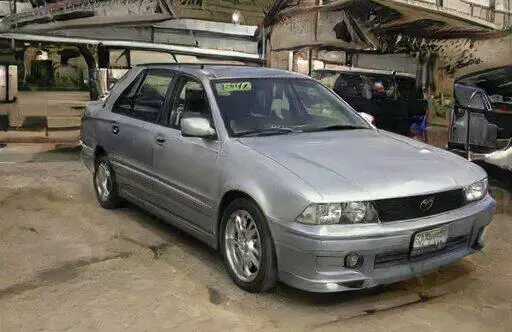 Automóvil sedán plateado en un taller mecánico, con llantas deportivas y detalles modernos. Ideal para los amantes de los coches.