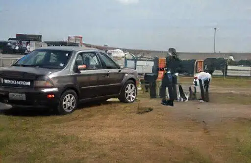 Vehículo gris estacionado en un taller al aire libre, donde un mecánico está revisando neumáticos en un entorno rural.